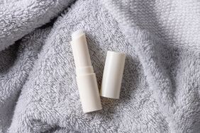 A lip balm tube with its cap removed, placed on a soft textured surface