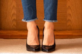 Women's legs in jeans and black high-heeled shoes on the floor of the house on the carpet near the door, women's shoes with heels