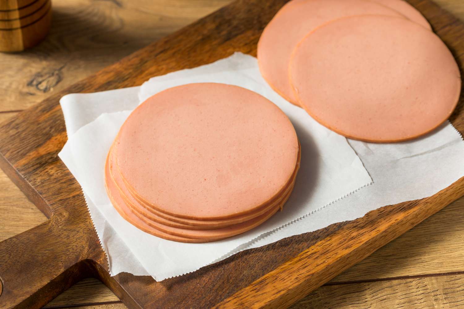 Slices of bologna on a wooden board with parchment paper