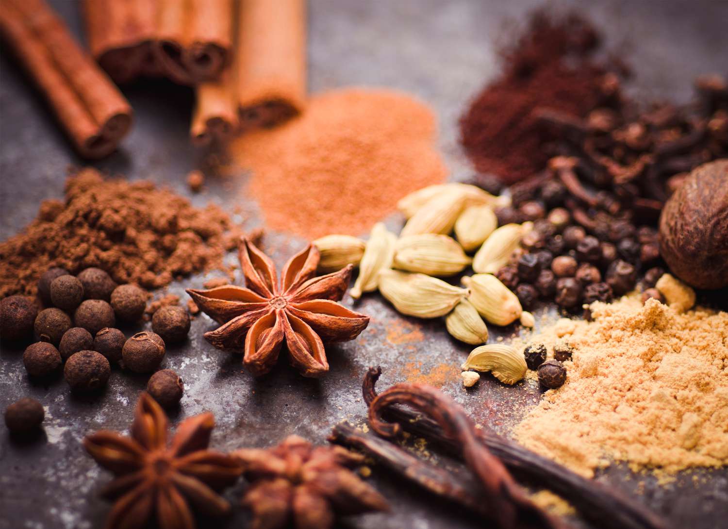loose spices, cinnamon sticks, cloves on a neutral surface