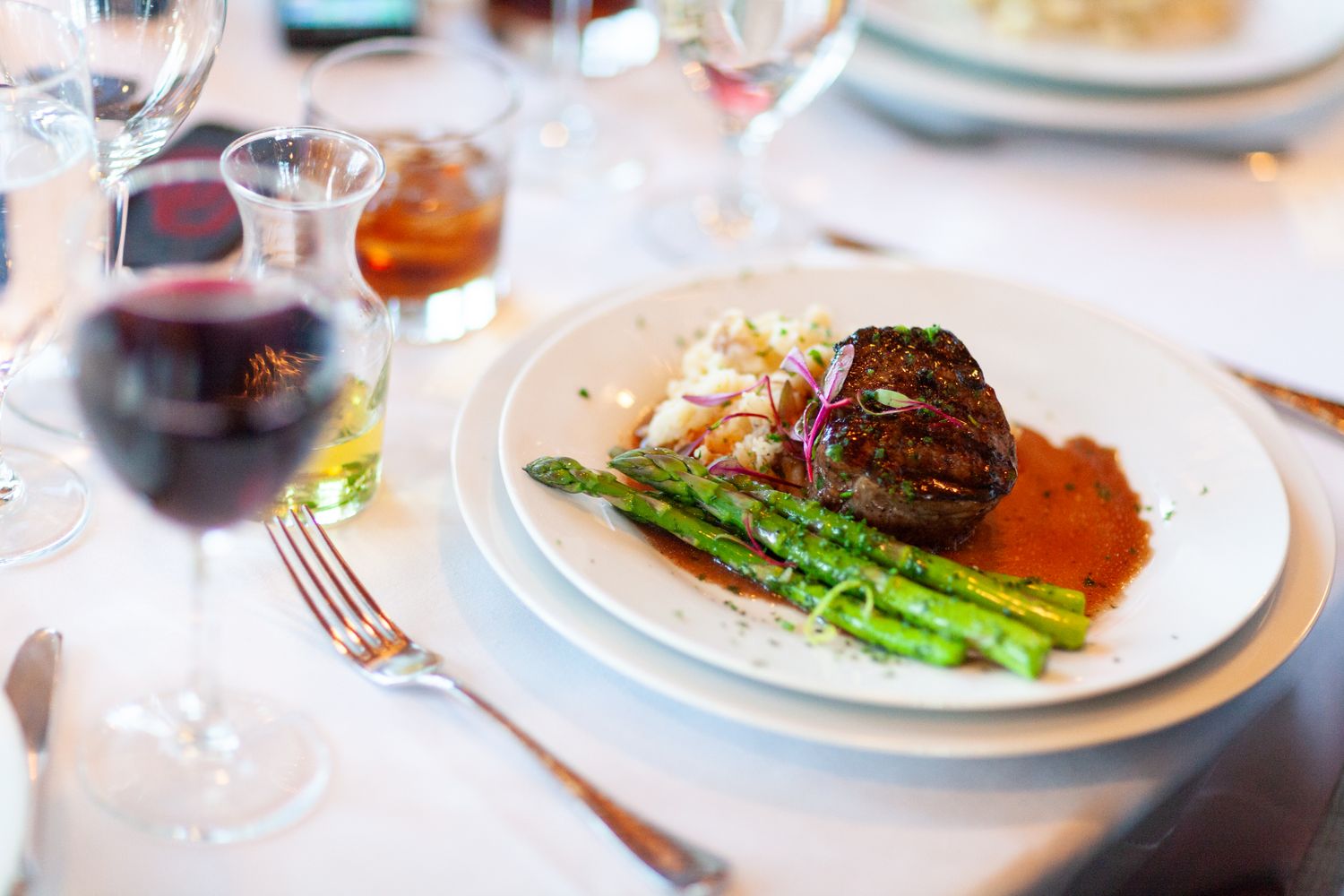 A plated meal featuring steak asparagus and mashed potatoes served with a glass of red wine on a dining table