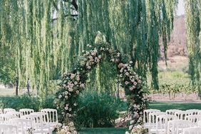 large greenery and pink floral wedding arch in front of willow tree