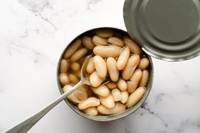 An open can of white beans with a spoon on a marble surface