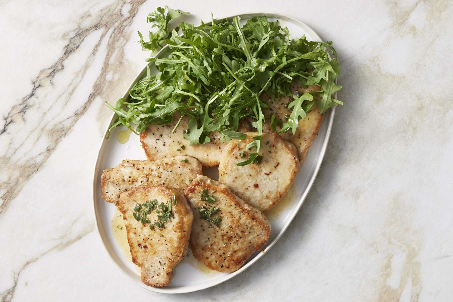 Pork scaloppine on white plate with dressed arugula 