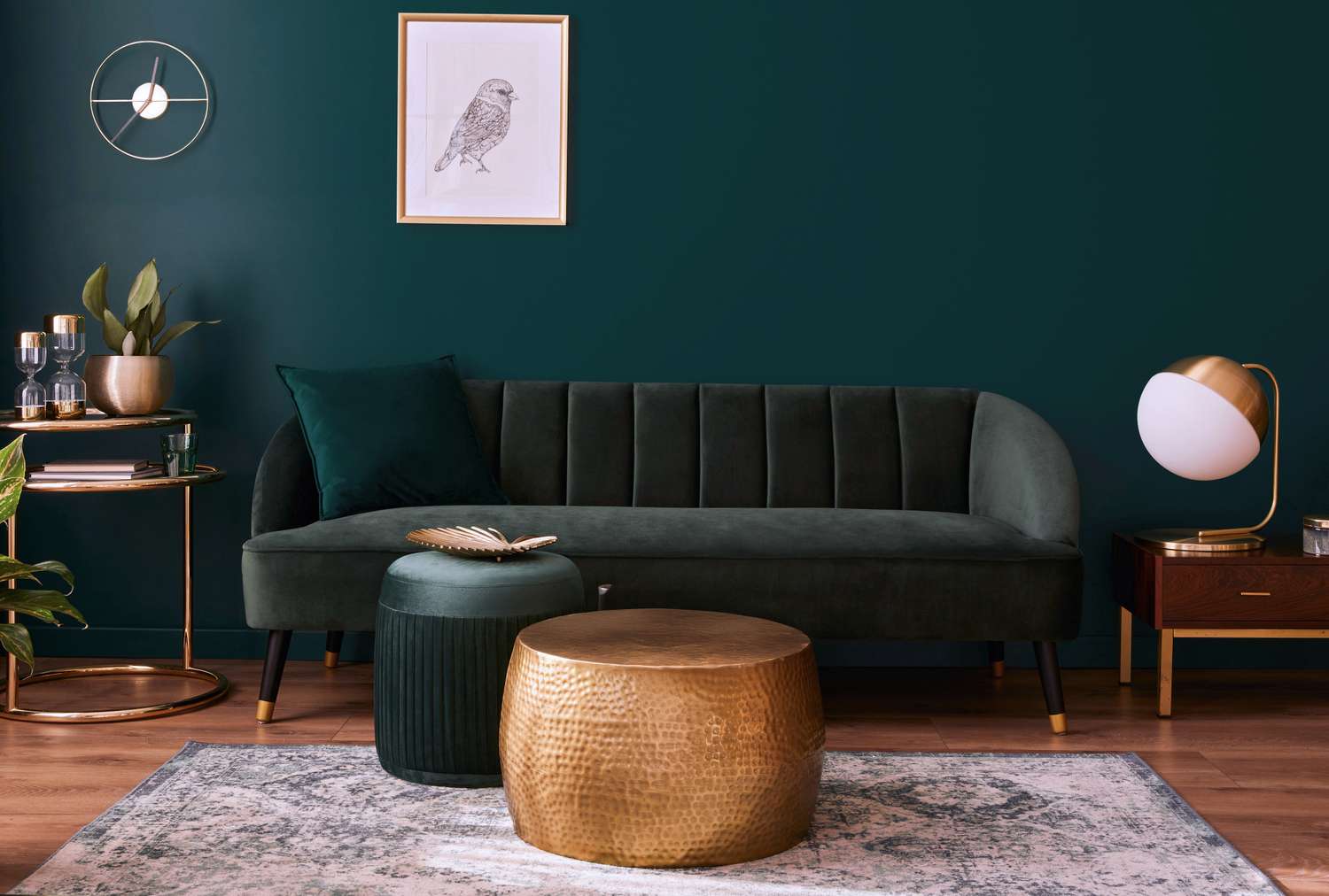 A stylish living room with a green sofa goldtone coffee table and accent furniture and a framed bird artwork on a dark wall