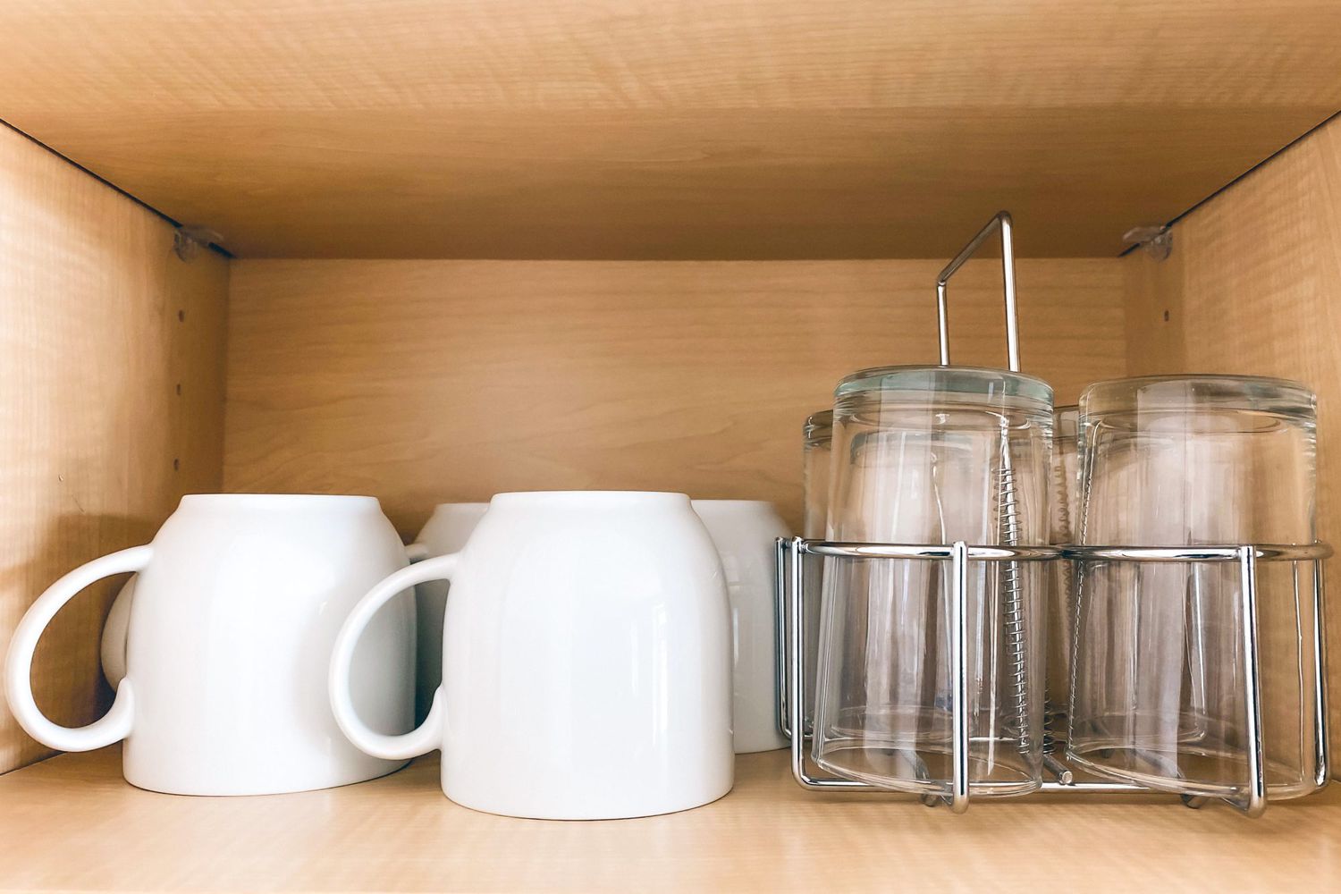 Close-up of cups and glasses neatly arranged facing down in kitchen cabinet