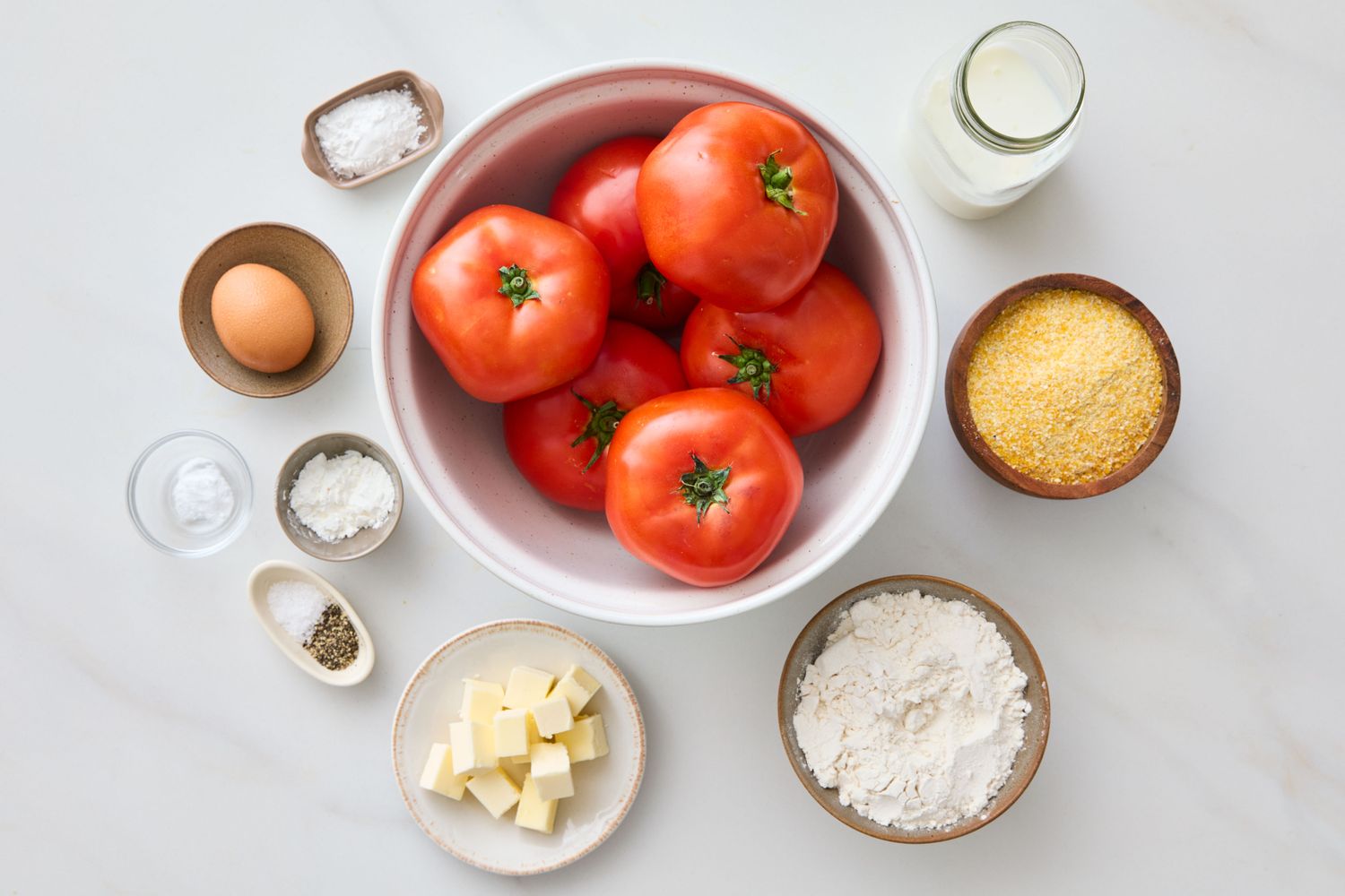 Ingredients arranged for making tomato cobbler including tomatoes flour cheese spices and milk