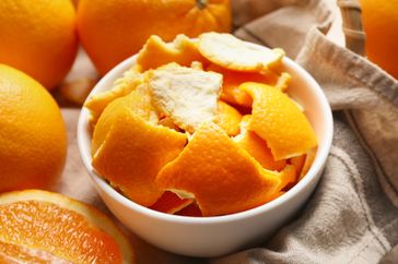 Bowl of orange peels surrounded by whole and sliced oranges