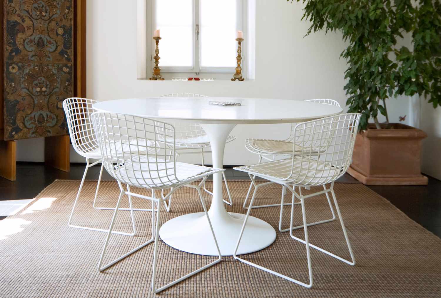 Round white table with wire chairs indoor setting with a carpeted floor and decorative backdrop