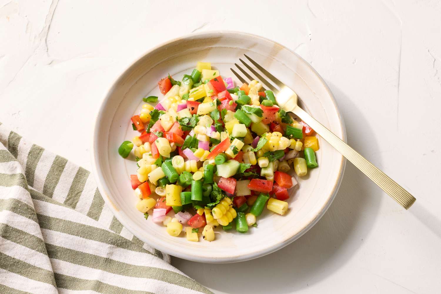 Chopped vegetable salad on a plate with a fork featuring a mix of diced fresh vegetables with a striped napkin nearby