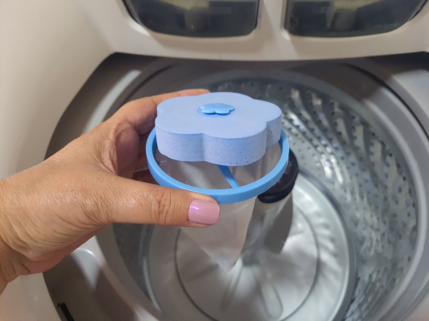 A hand holds a laundry filter next to a washing machine drum