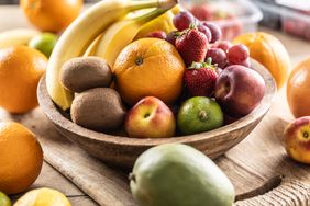 A wooden bowl filled with a variety of fresh fruits including bananas oranges kiwis strawberries limes and apples