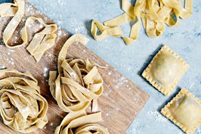 Freshly made pasta including tagliatelle and ravioli on a wooden board and a light surface dusted with flour