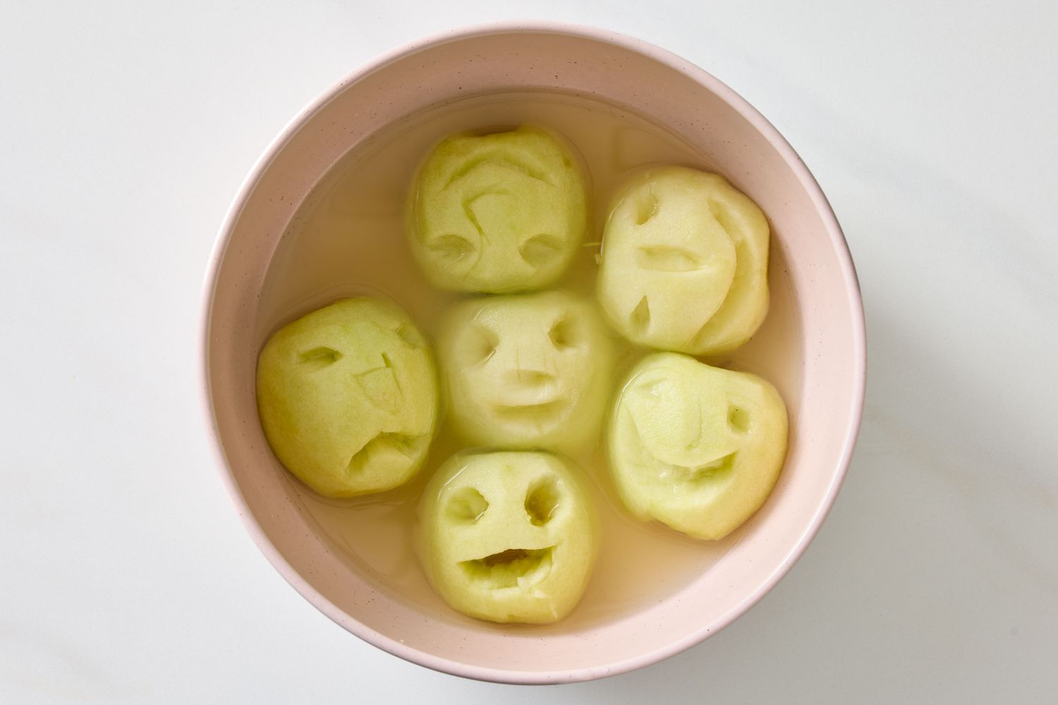 Carved apple faces soaking in a bowl of liquid styled to resemble shrunken heads