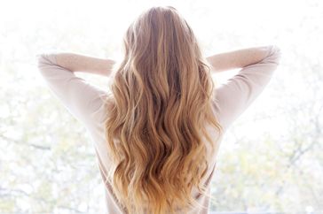 Person with long wavy hair viewed from behind arms raised