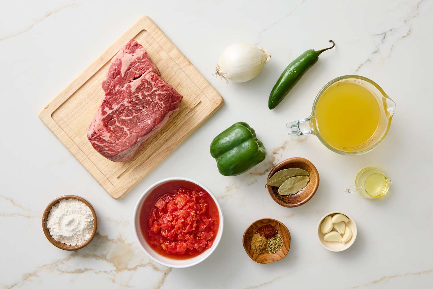 Ingredients for cooking carne guisada on a surface including beef vegetables and seasonings