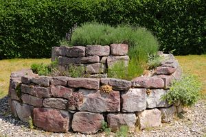 A circular raised garden bed made of stacked stones planted with various herbs and small plants