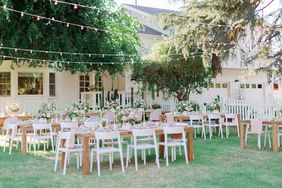 long wooden tables outdoors with white chairs and overhead string lights