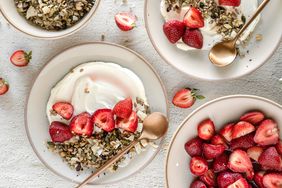 Bowls with yogurt granola and strawberries along with a bowl of strawberries and spoons