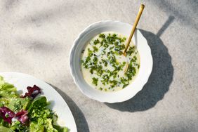 A bowl of buttermilk herb vinaigrette with a golden spoon and a portion of salad on a white plate