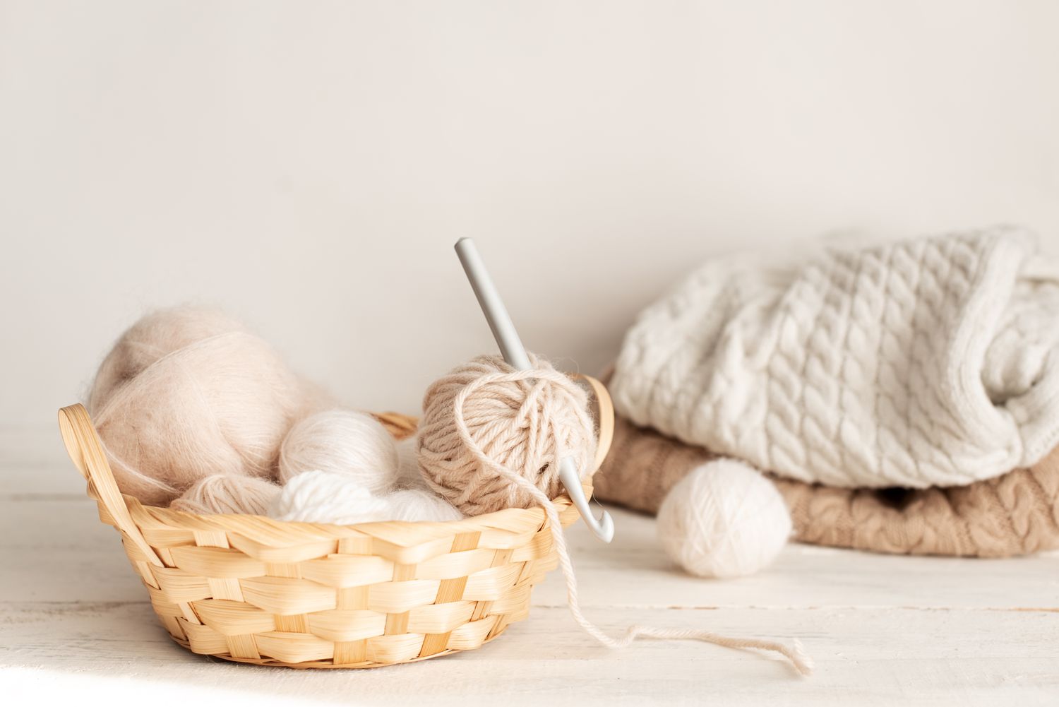 Vintage knitting needles, scissors and yarn inside old wire basket on wooden stool, still life photo with soft focus