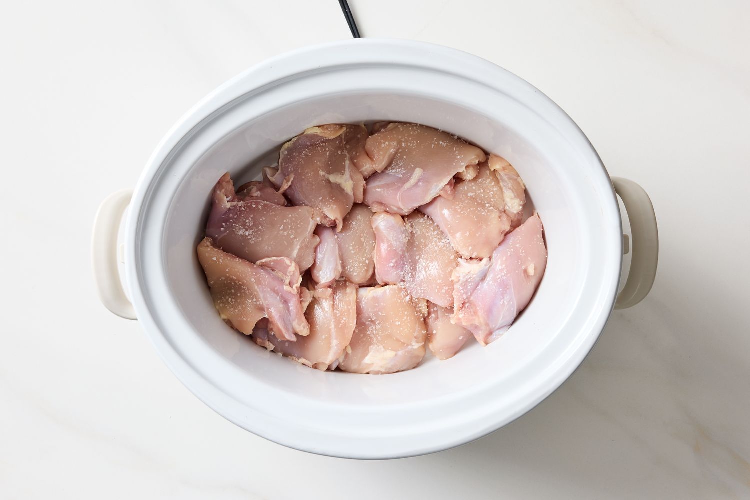 Chicken pieces in a slow cooker arranged evenly and ready for cooking