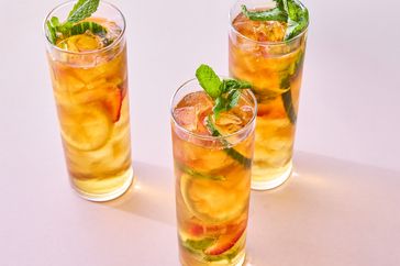 Three glasses of a fruit garnish and herbdecorated beverage on a light background