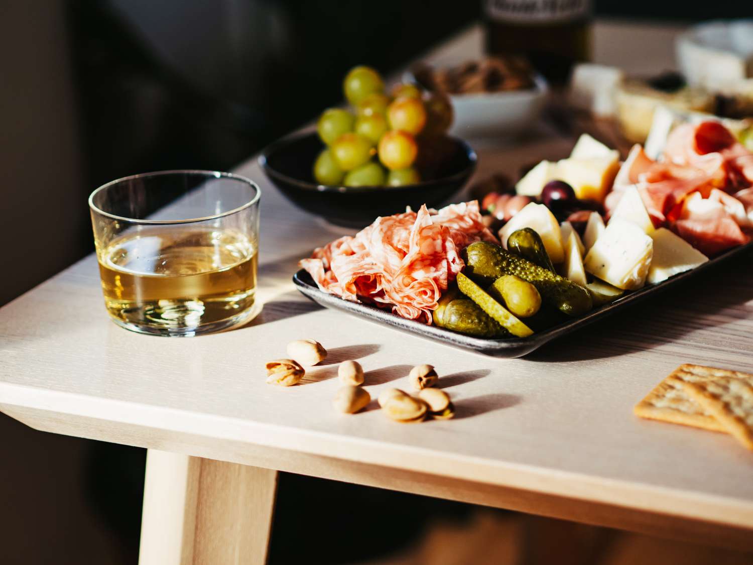 Charcuterie platter with meats cheeses crackers gherkins and a drink on a table