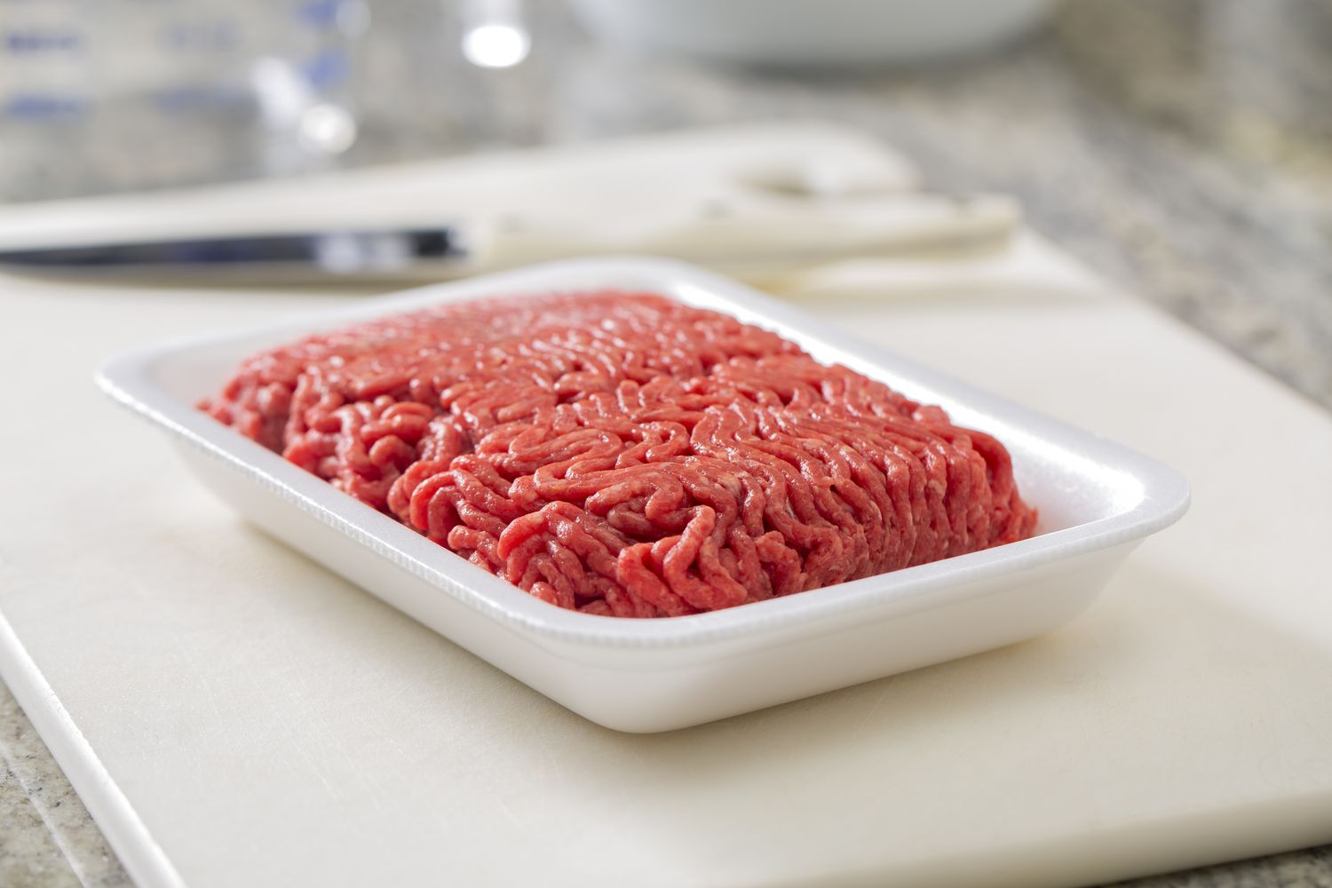 A package of raw ground beef on a white surface with a knife in the background