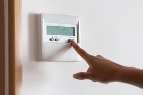 A hand adjusting a digital thermostat control panel on a wall selecting or setting a temperature