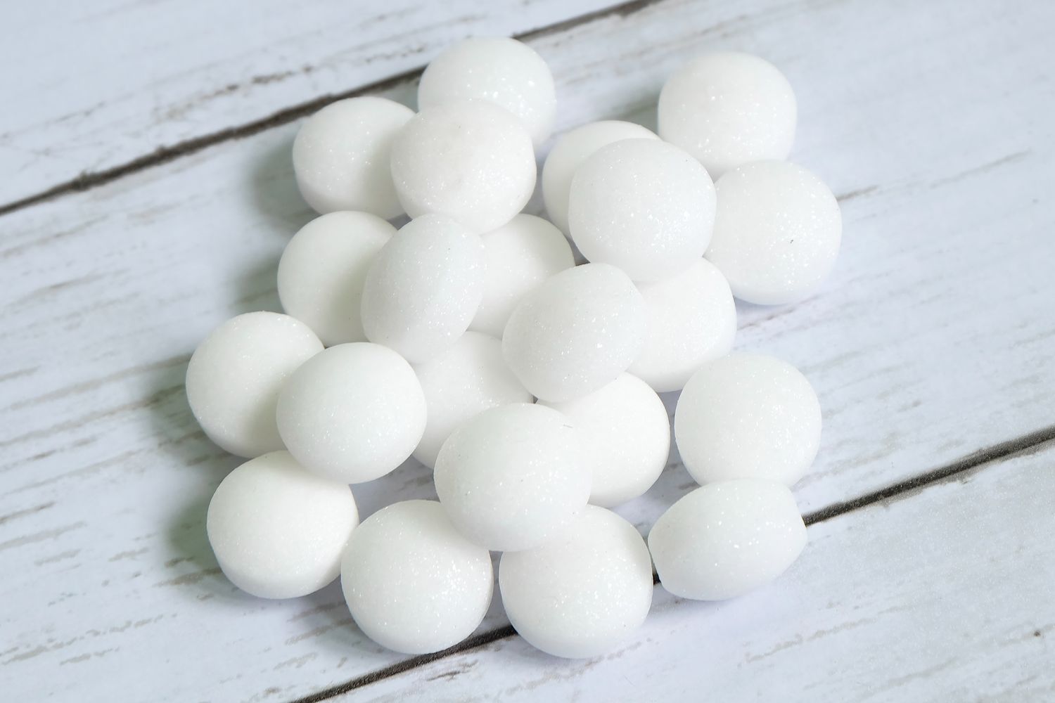 Stack of white round mothballs on a wooden surface