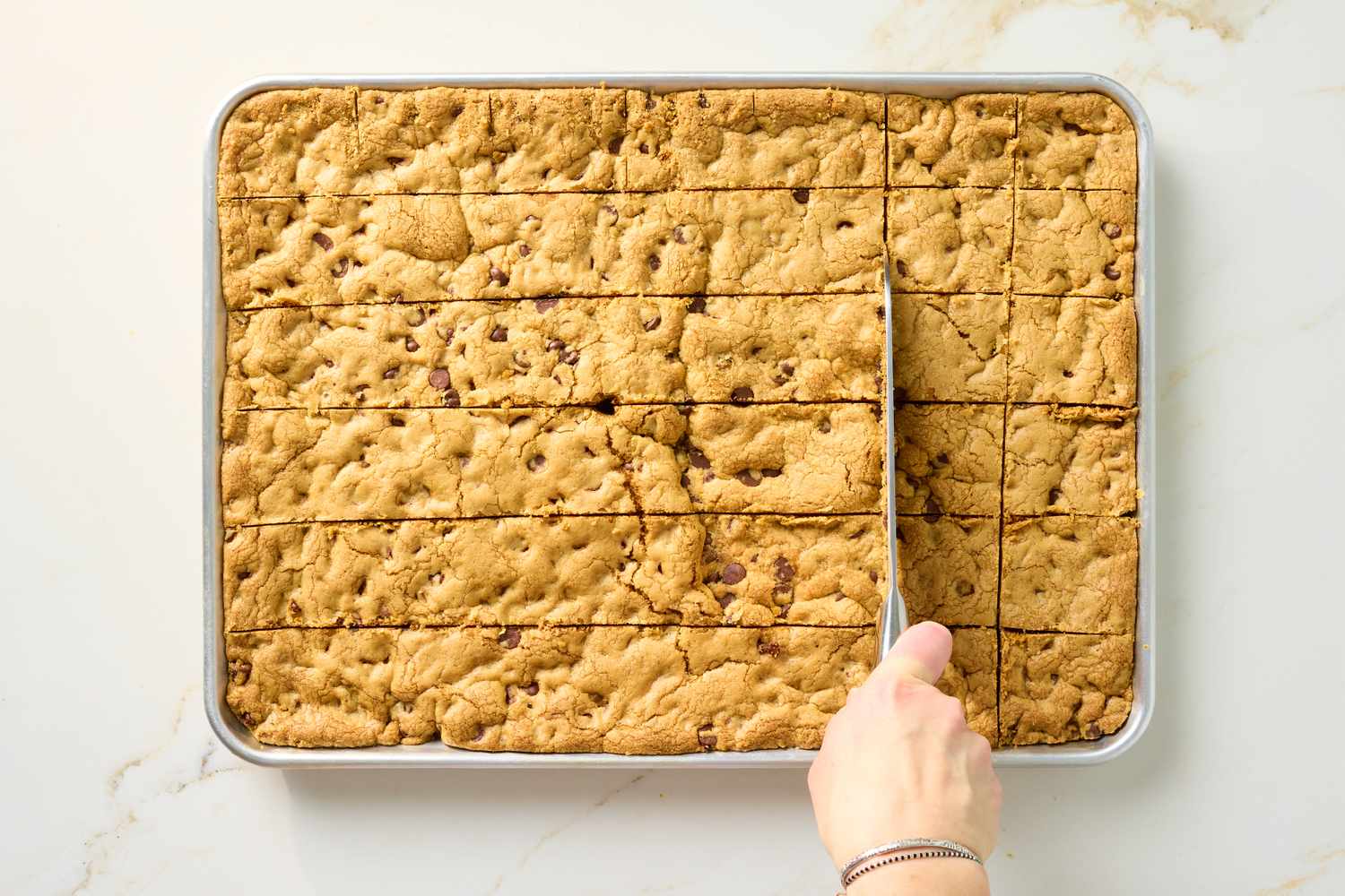 A tray of chocolate chip cookie bars being sliced with a knife