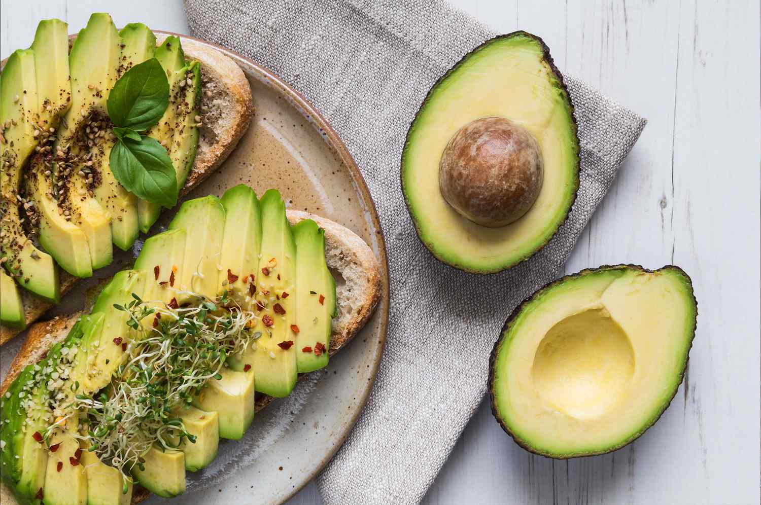 Avocado toast and a halved avocado on wooden table
