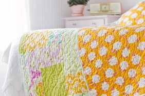 Quilt spread on a bed in a brightly lit room featuring a patchwork design with geometric patterns