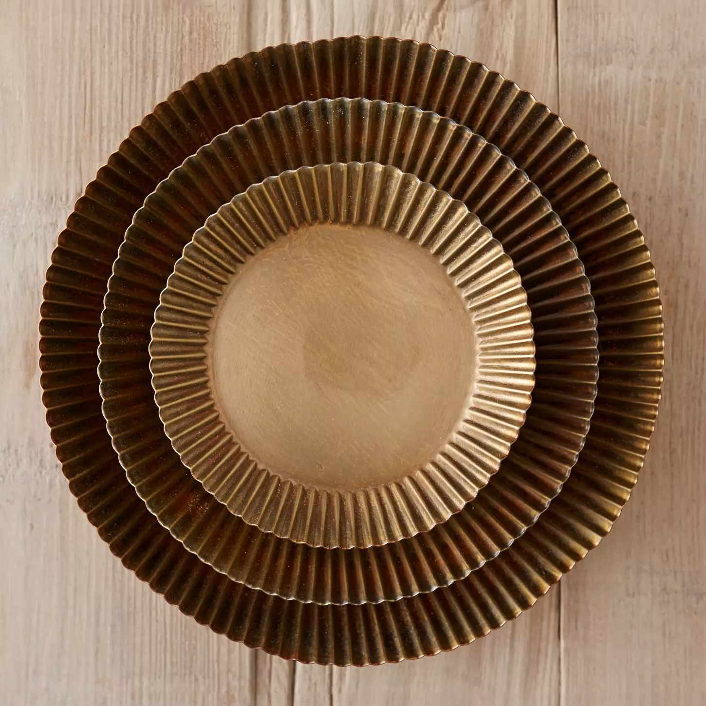 Three nested plates with fluted edges positioned on a wooden surface