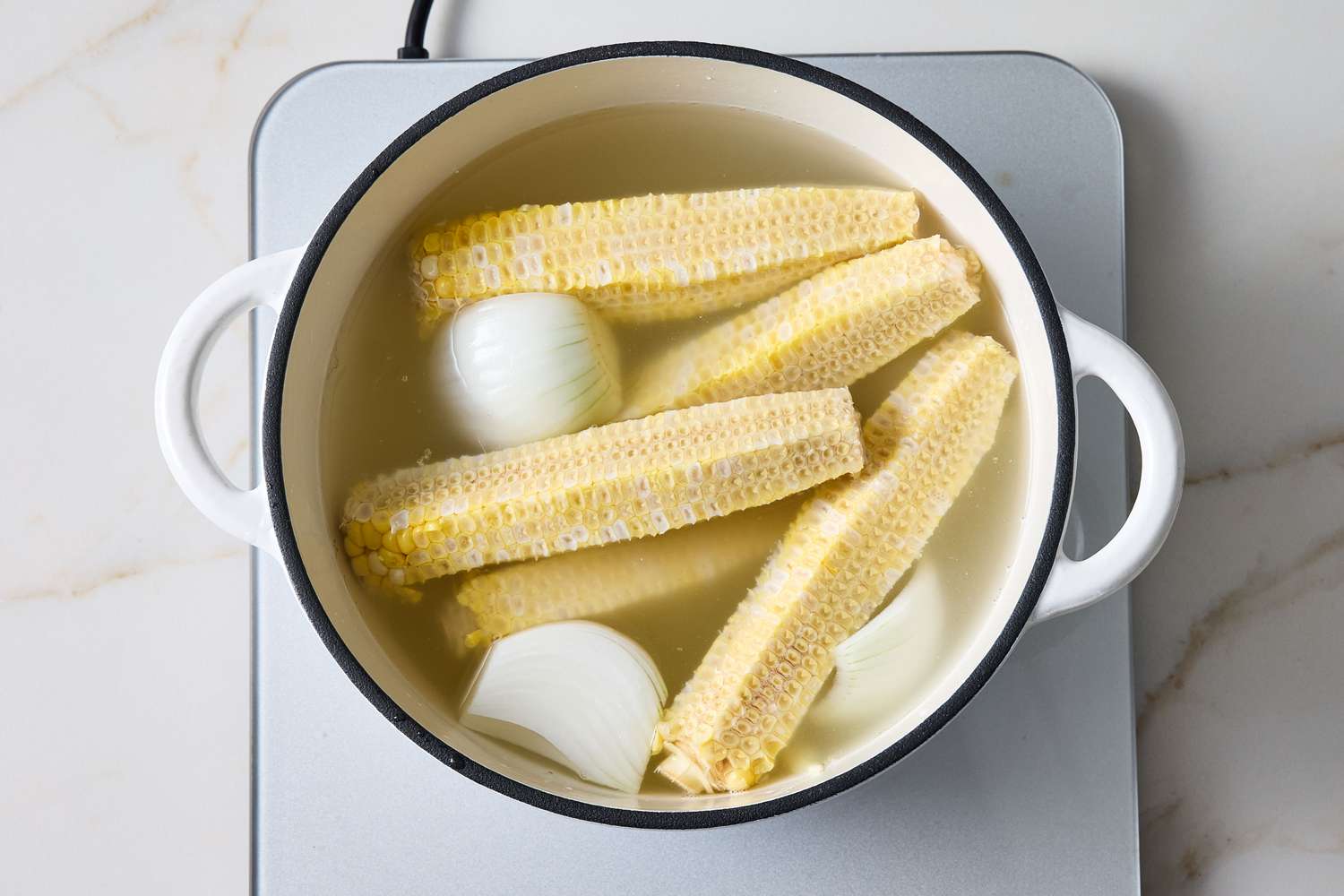 Corn cobs and onion sections boiling in a pot on a stovetop