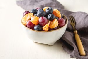 A bowl of assorted fruits, including grapes, blueberries, and mandarin slices, on a table with a fork placed nearby
