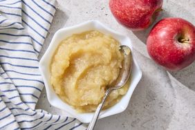 Bowl of applesauce with a spoon next to two apples