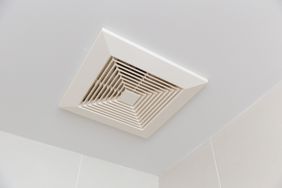 A ceilingmounted ventilation fan with a louvered grille in a room corner