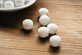 Several small spherical objects likely mothballs on a wooden surface with a plate partially visible in the background