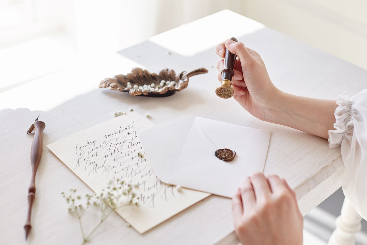 A handwritten letter and an envelope being sealed with a wax stamp on a table