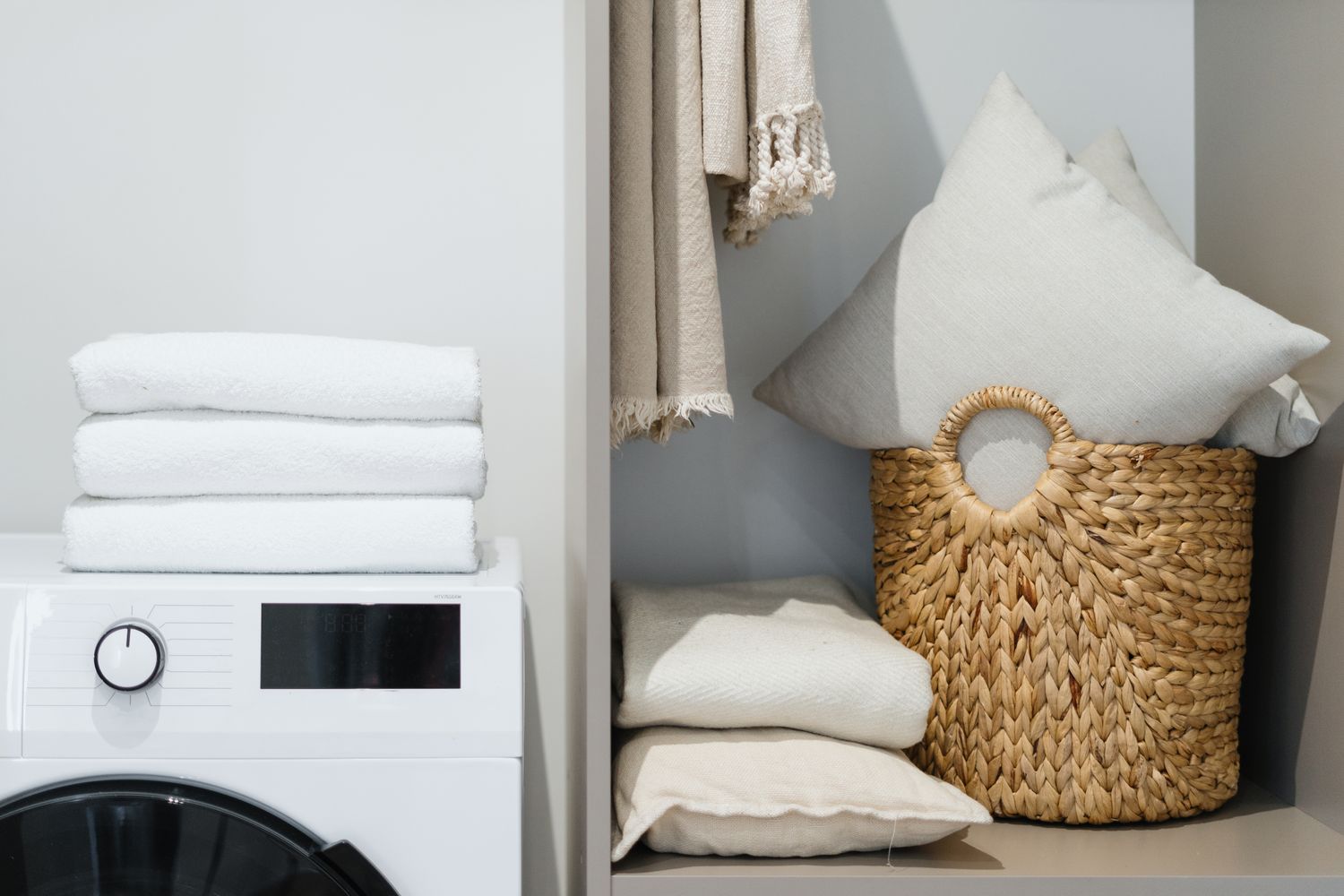 Laundry corner with folded towels a washing machine and a woven basket with pillows