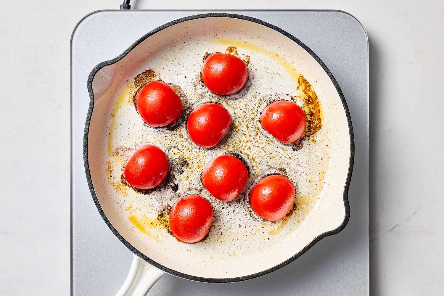 A skillet with tomatoes being cooked arranged evenly on the surface