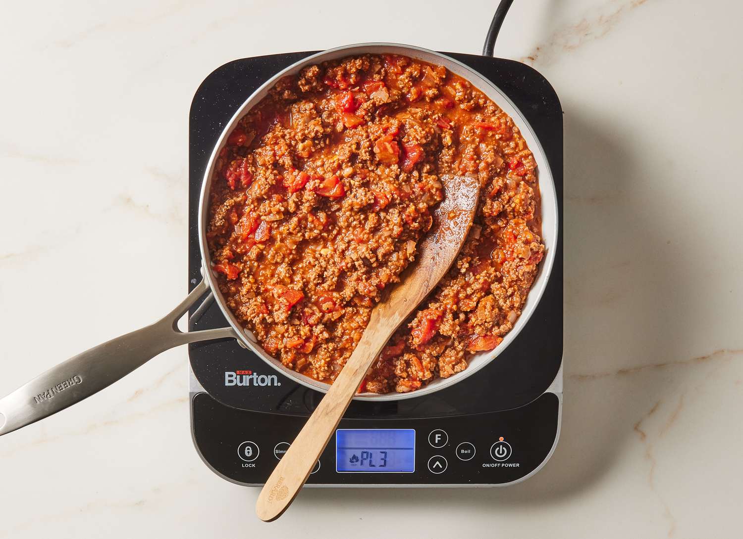 meat and tomato sauce cooking in a skillet with a wooden spoon