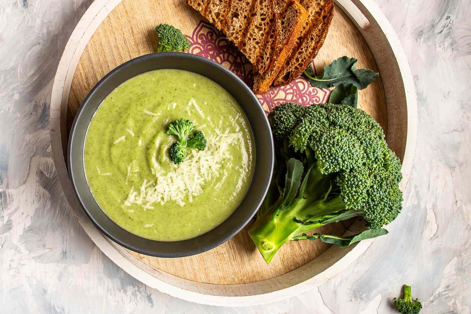 Bowl of green soup garnished with broccoli served on a tray with bread and fresh broccoli