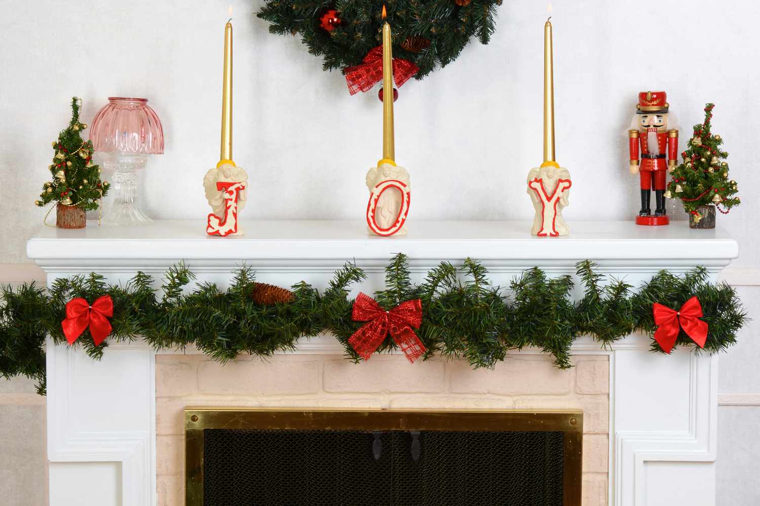 Holidaythemed mantle decorated with candles spelling JOY greenery a nutcracker and small Christmas trees