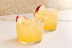 Two glasses of a cocktail garnished with slices of red apple