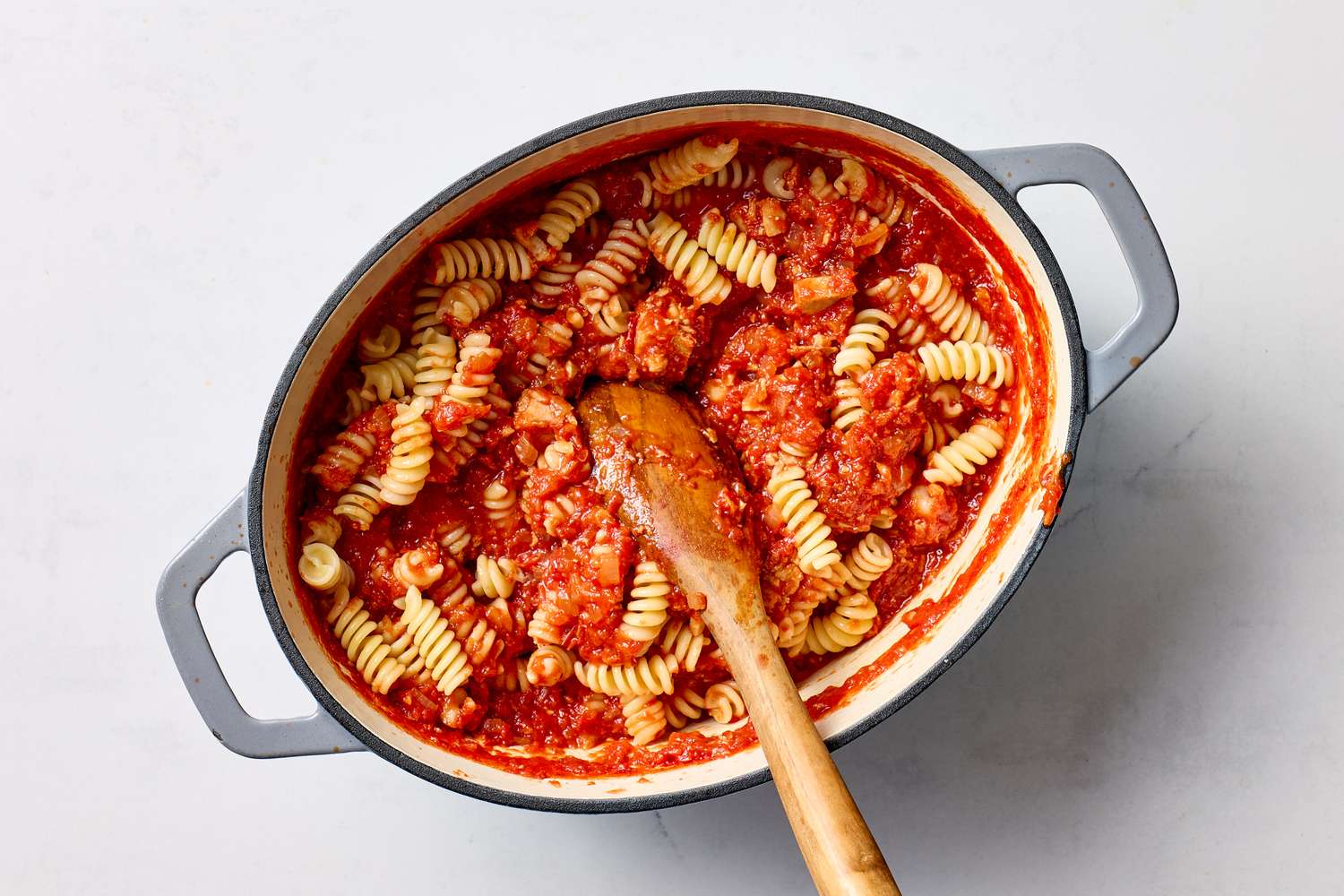 A pot of spiral pasta mixed with a tomatobased sauce a wooden spoon placed inside