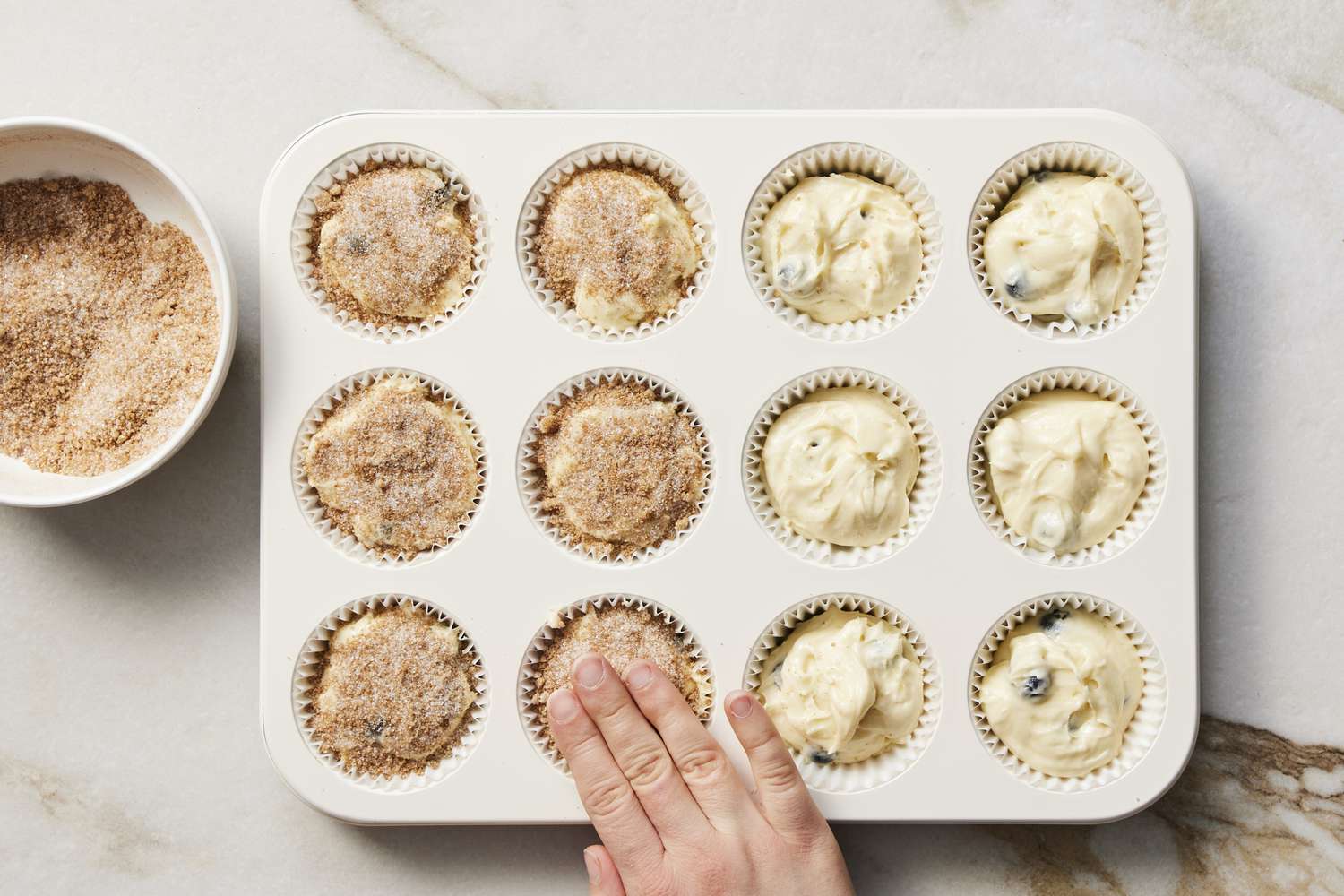 Patting down topping on blueberry cupcakes in pan