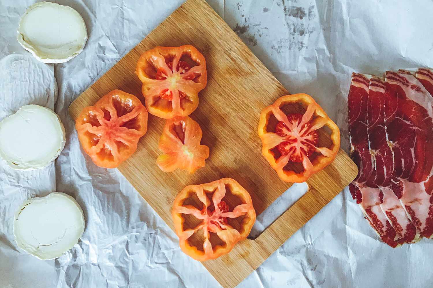 Sliced tomatoes and meat on a board with cheese rounds